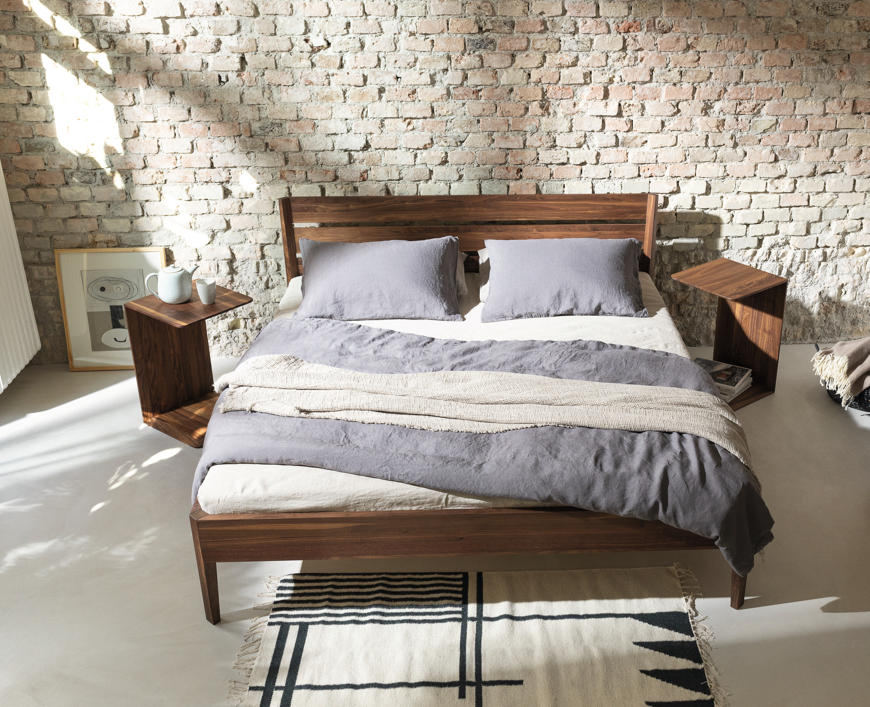 Light Bett von Team 7, Massivholz dunkelbraun, mit blauer Bettwäsche in Schlafzimmer mit Backsteinwand