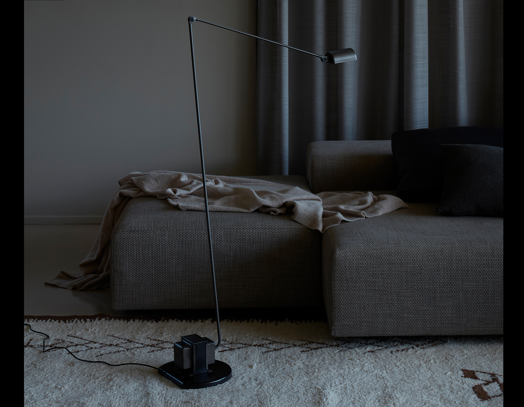 Moderne Stehleuchte Daphine von Terra Lumina in Schwarz, minimalistische Bogenform über grauem Polstersofa in Wohnraum-Szenerie.